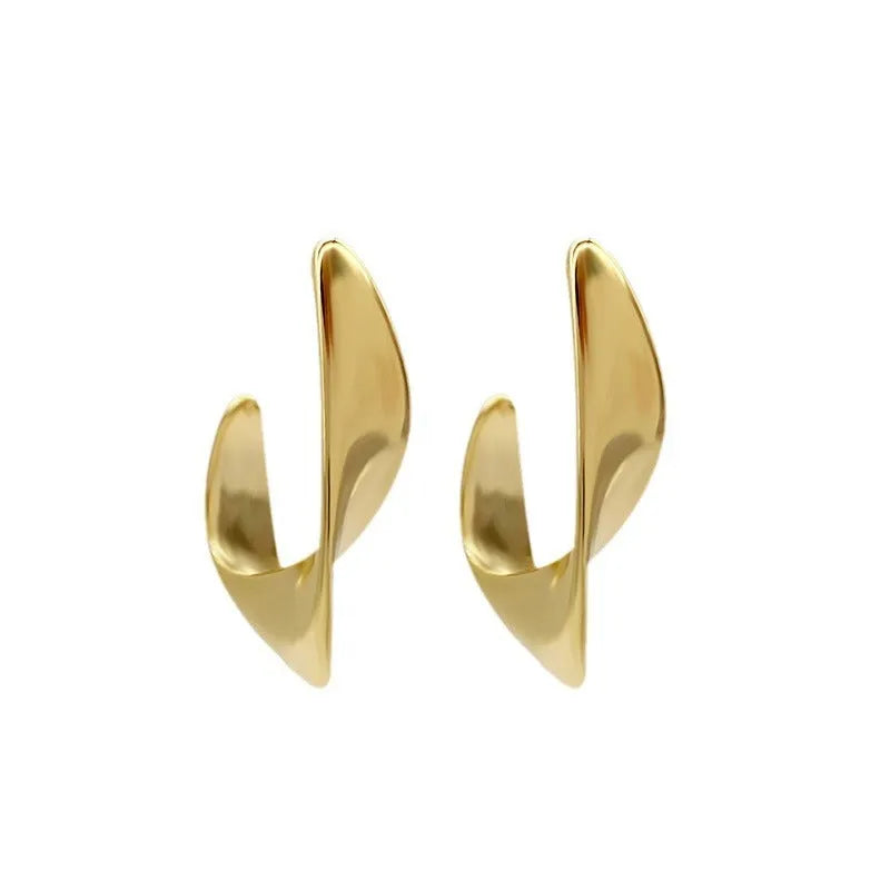 A pair of gold twisted geometric metal earrings with a round detail on a white background.