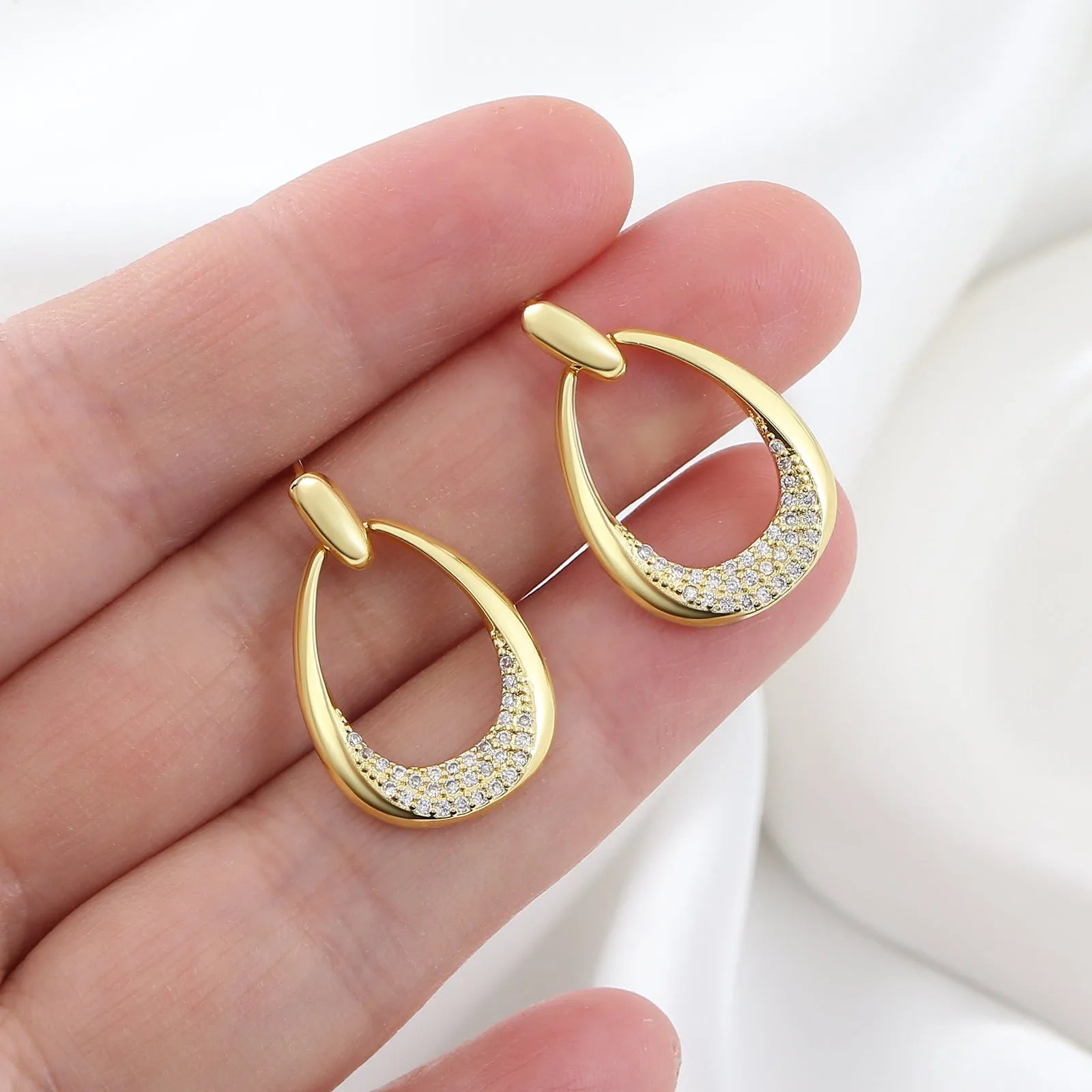 Women's yellow gold geometric drop earrings with oval and round elements on a white background.