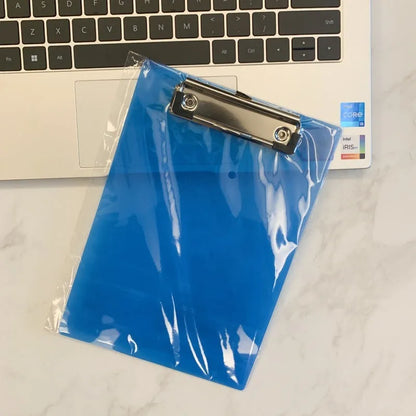 Transparent A4 plastic plate holder with metal clip, holding white paper, on a desk.