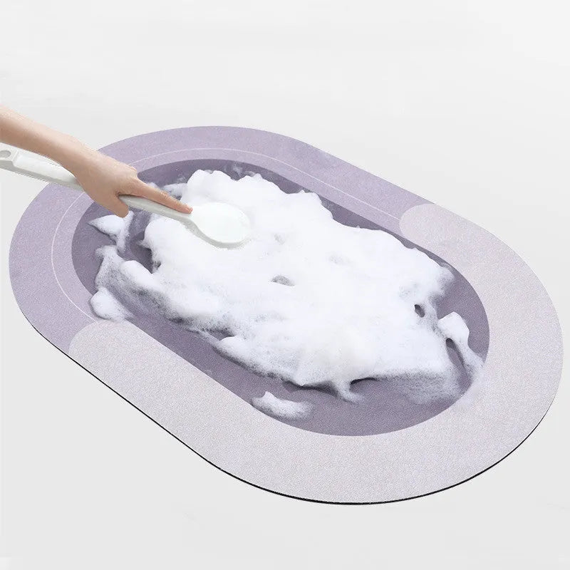 Oval grey bath mat with non-slip rubber bottom on a tiled floor, showing absorbent fabric surface