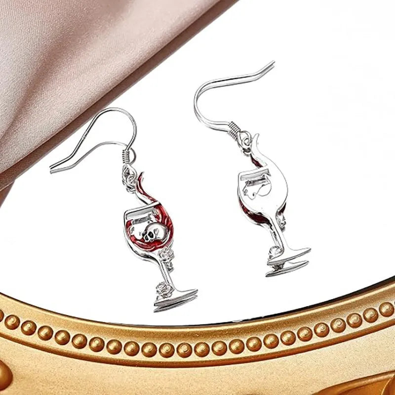 Close-up of a pair of silver-toned geometric earrings combining a skull motif with a wine glass shape.