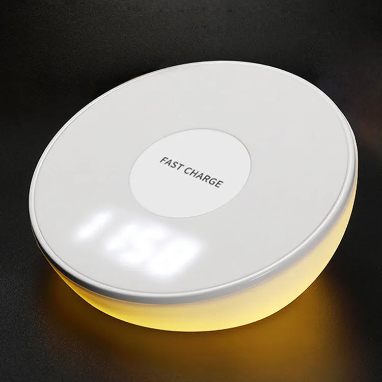 White wireless charging pad with digital clock display and three control buttons on a bedside table.