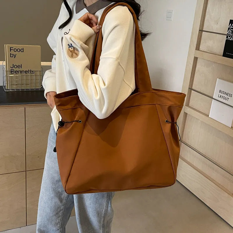 Commuter shoulder tote bag made from soft Oxford cloth, featuring a convenient folding design and street trend styling, available in five colours including black, light grey, dark grey, brown, and purple.