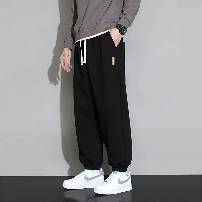 Man wearing loose grey sports trousers with an elasticated drawstring waistband.