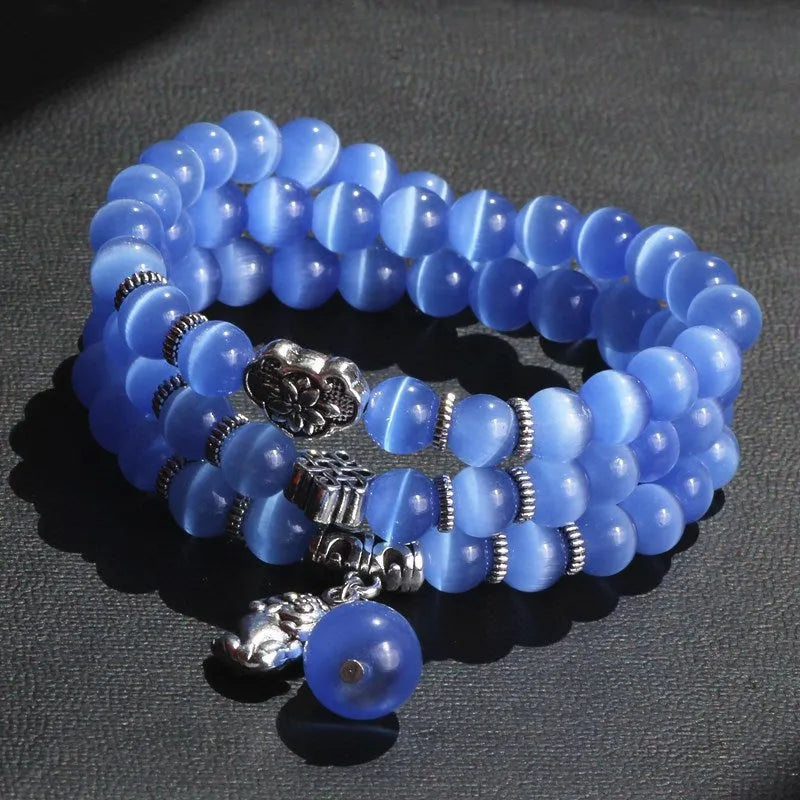 Close-up of a women's opal cat eye bracelet with three geometric rings and a lucky cat charm on a long, adjustable cord.