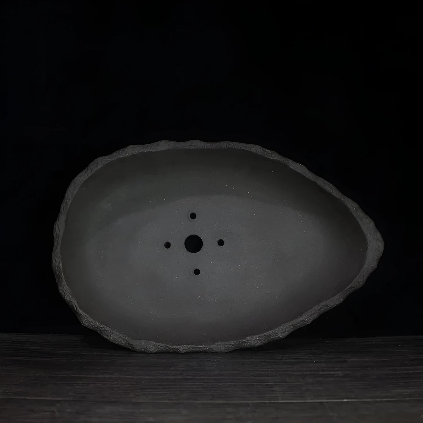 Handmade purple clay flower pot in a creative shape on a floor.