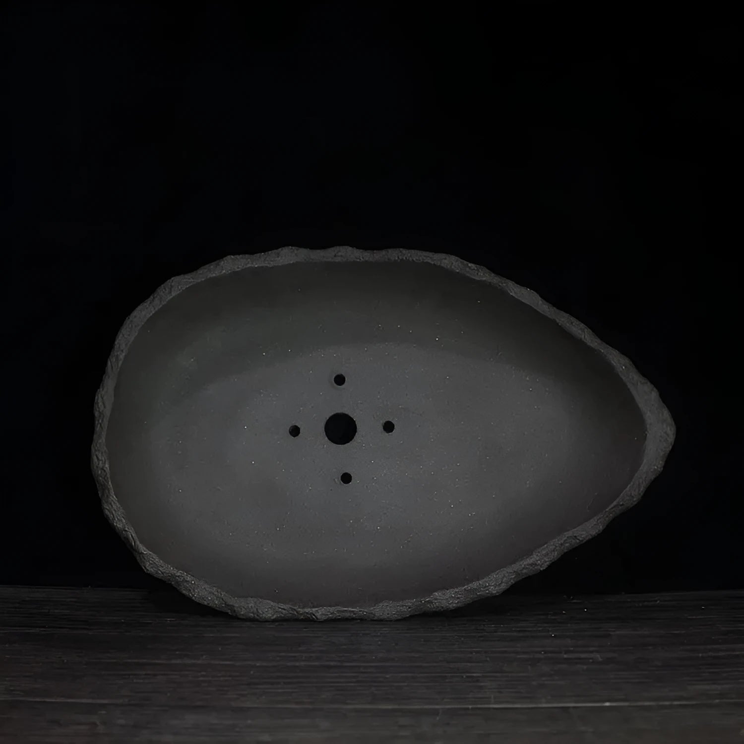 Handmade purple clay flower pot in a creative shape on a floor.