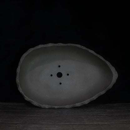 Handmade purple clay flower pot in a creative shape on a floor.