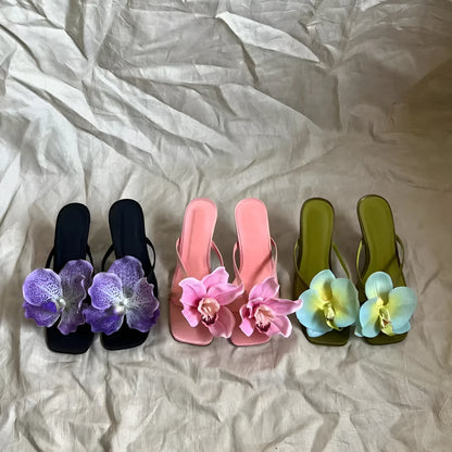 Pink women's sandals with a satin upper, artificial white Phalaenopsis flower, square toe, and a mid-height heel.