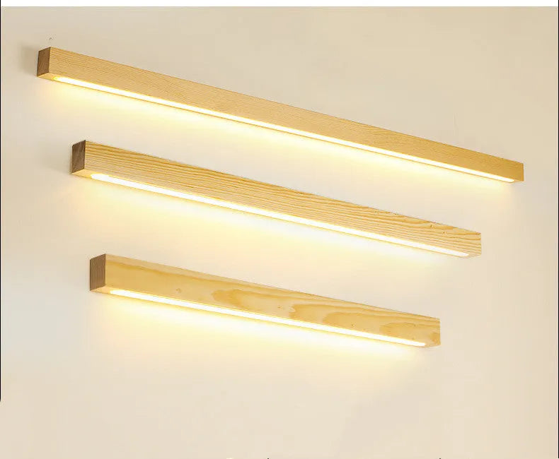 Slim walnut-coloured wooden strip wall lamp with acrylic light diffuser mounted on a plain wall.