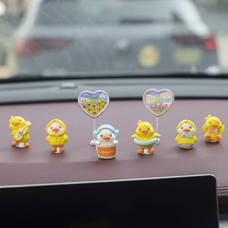 Set of six small yellow PVC duckling car decorations and one cartoon sign on a car dashboard.