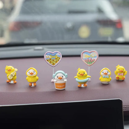 Set of six small yellow PVC duckling car decorations and one cartoon sign on a car dashboard.