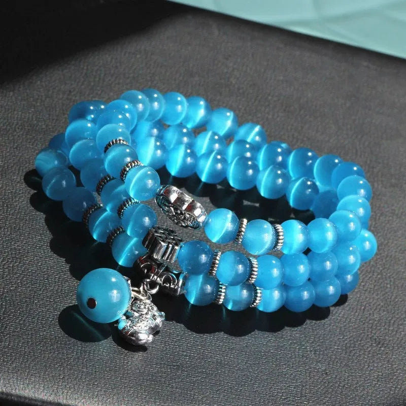 Close-up of a women's opal cat eye bracelet with three geometric rings and a lucky cat charm on a long, adjustable cord.