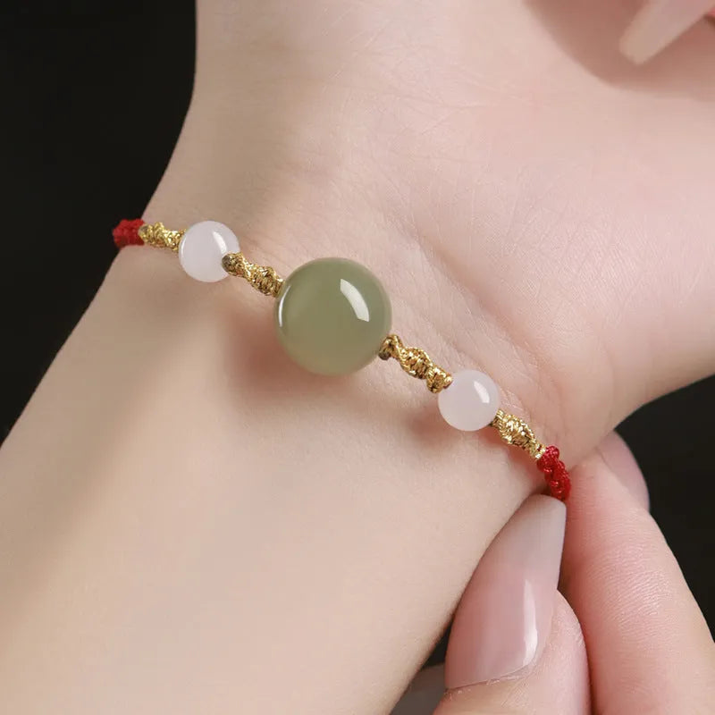 Hand-woven red rope bracelet with Hetian jade lucky beads on a wrist.