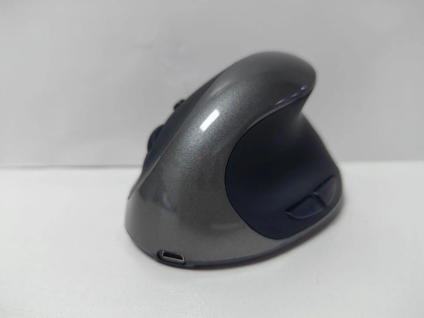 Ergonomic vertical mouse in black, shown next to a laptop, highlighting its unique upright shape and USB receiver.