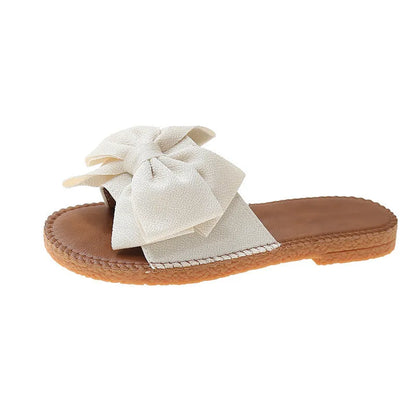 Women's beige suede slip-on sandals with a bow detail and soft rubber flat sole.