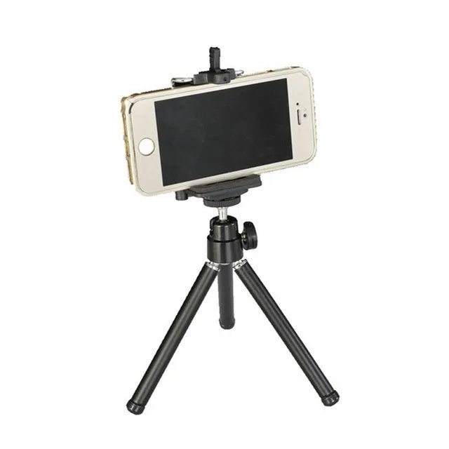 Black mini camera tripod with extended legs and a separate U-shaped universal phone clip on a table.