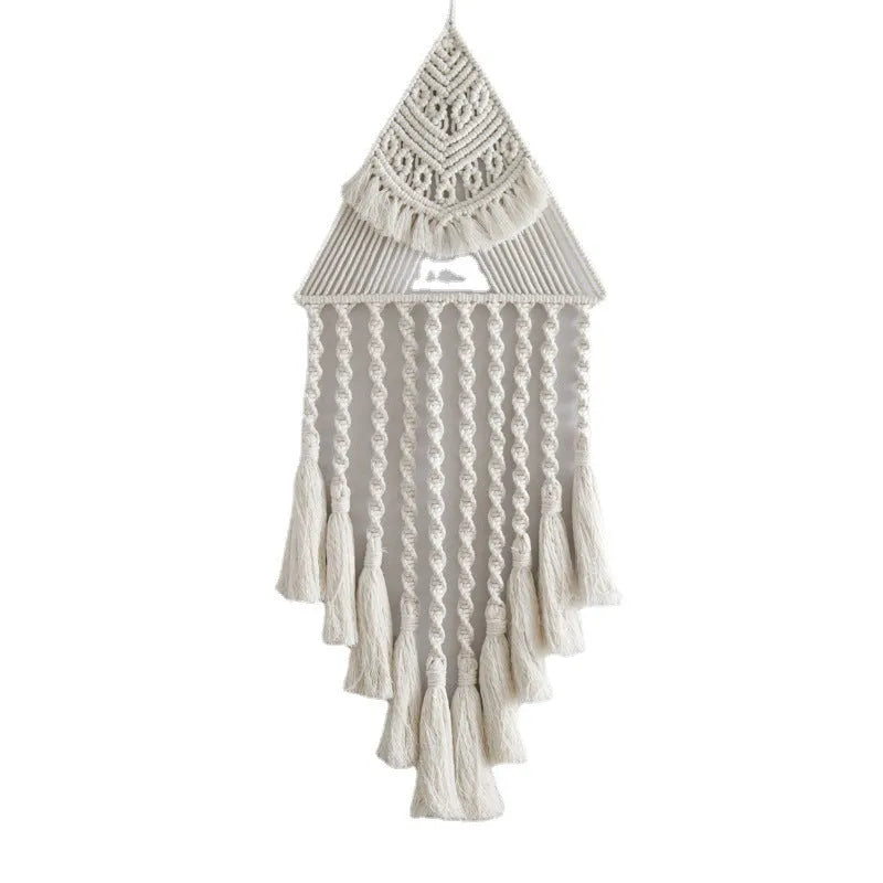 Large white handwoven triangle dream catcher pendant with wooden beads and a long tassel hanging on a wall.