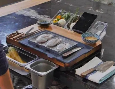 Bamboo cutting board with smooth surface alongside two large and three small plastic storage trays for vegetables and meat.