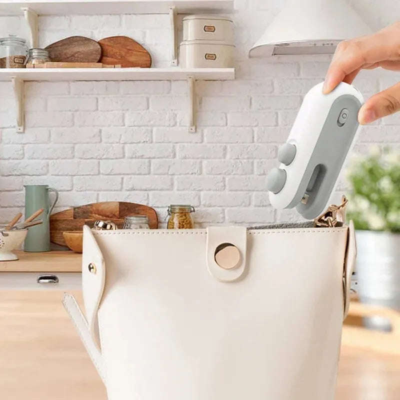 Handheld white portable heat sealer with USB Type-C port and magnetic back on a metal surface.