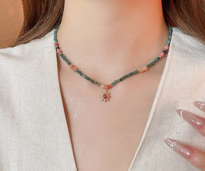 Geometric sun stone pendant on a freshwater pearl necklace with gold and blue electroplated finish.