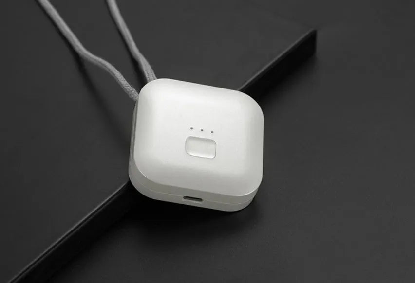 Small pink wearable air purifier pendant on a necklace, showing USB charging port and single button.