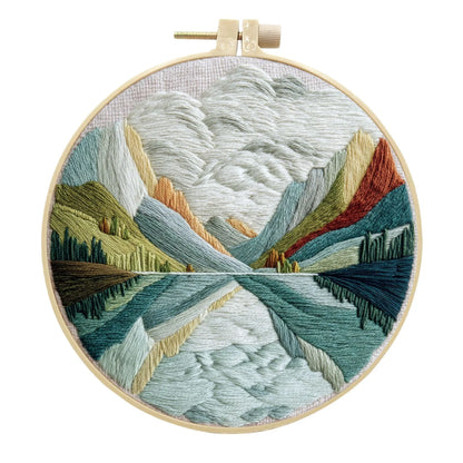 Complete DIY embroidery kit with 15cm bamboo frame, pre-printed landscape fabric, threads, and needles laid out.
