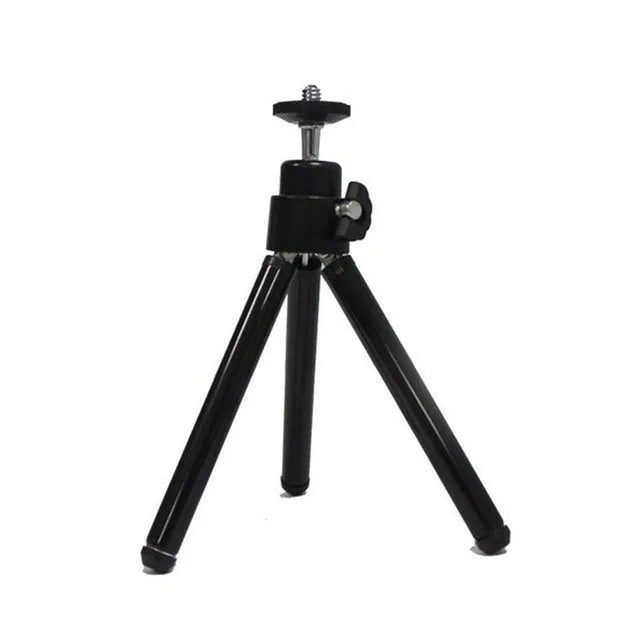 Black mini camera tripod with extended legs and a separate U-shaped universal phone clip on a table.