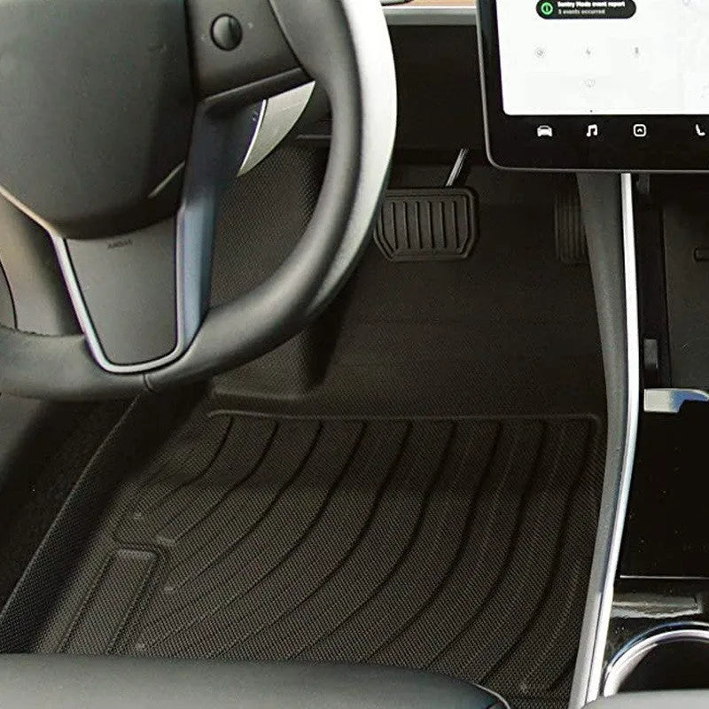 Custom black rubber floor mats with textured surface and TPE driver's footrest, fitted in a Tesla interior.