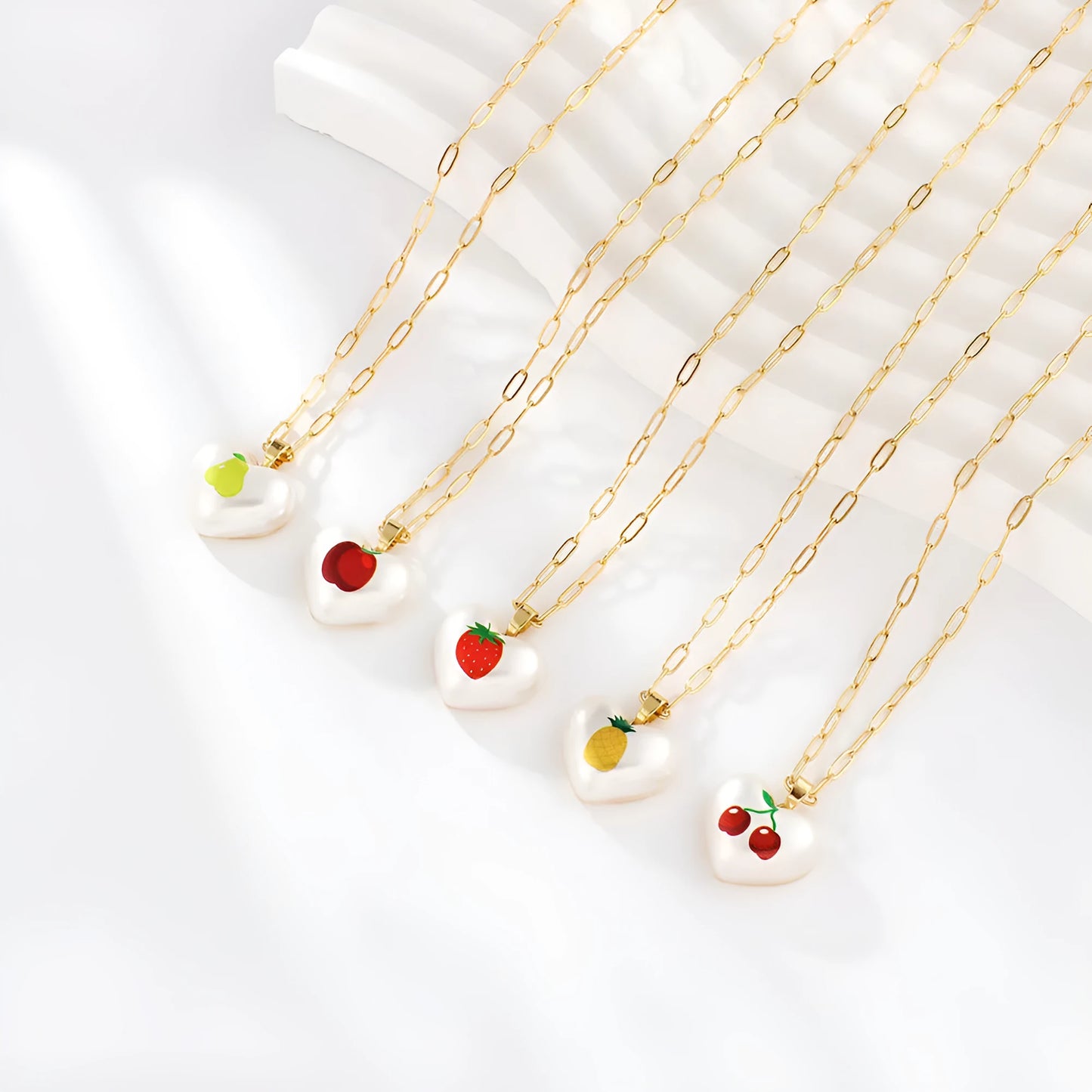 Geometric fruit heart pendant necklace on an adjustable chain, showing strawberry, pineapple, apple, pear, and cherry design options.