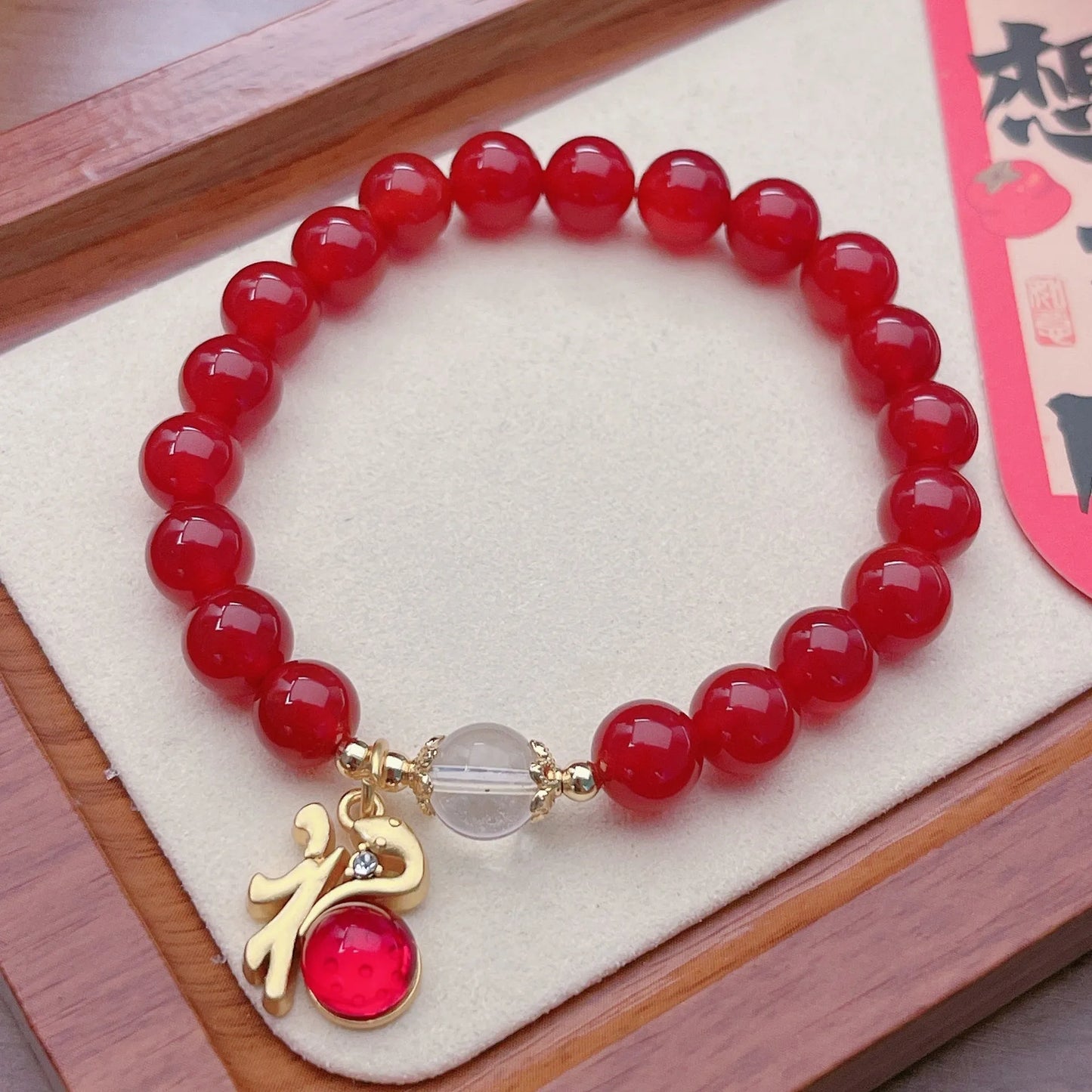 Close-up of a red agate bracelet with a dragon charm and Lucky Bag symbol on a wrist.