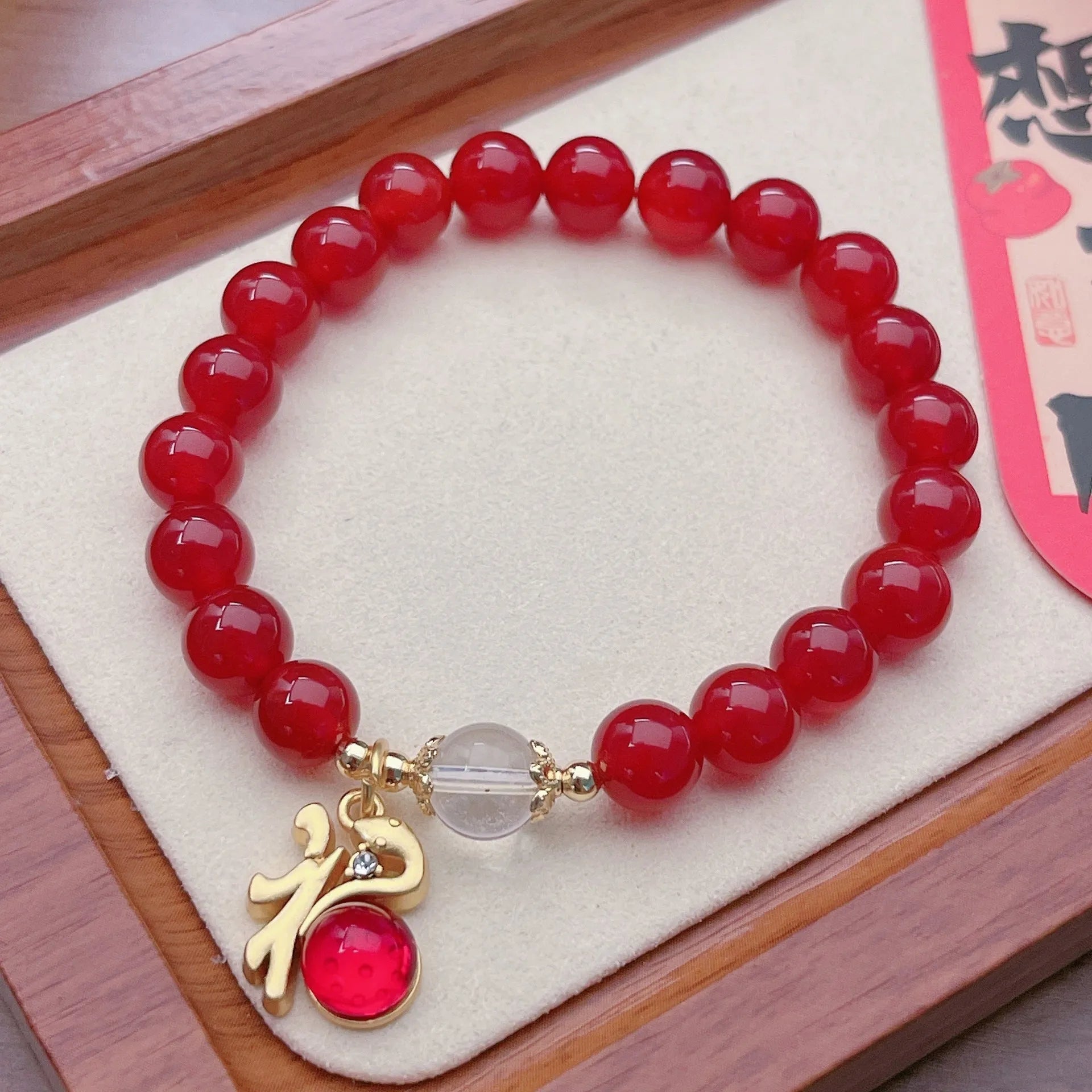 Close-up of a red agate bracelet with a dragon charm and Lucky Bag symbol on a wrist.