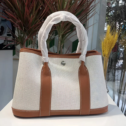 Canvas and leather tote bag in bucket shape with crossbody strap, shown in black, brown, gray or red colour options