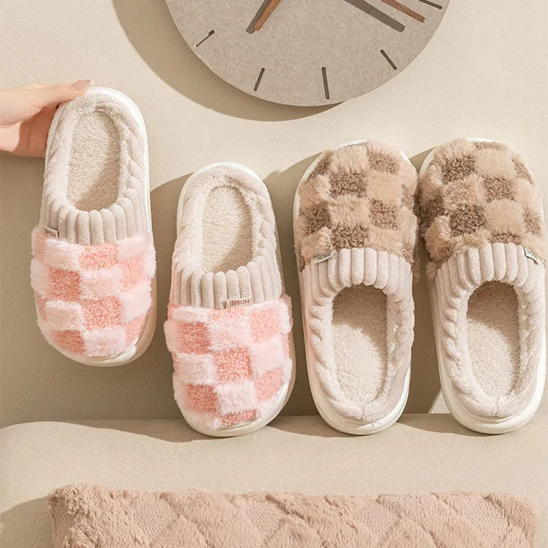 Plaid pattern women's plush slippers with coral velvet upper and textured PVC sole on a wooden floor.