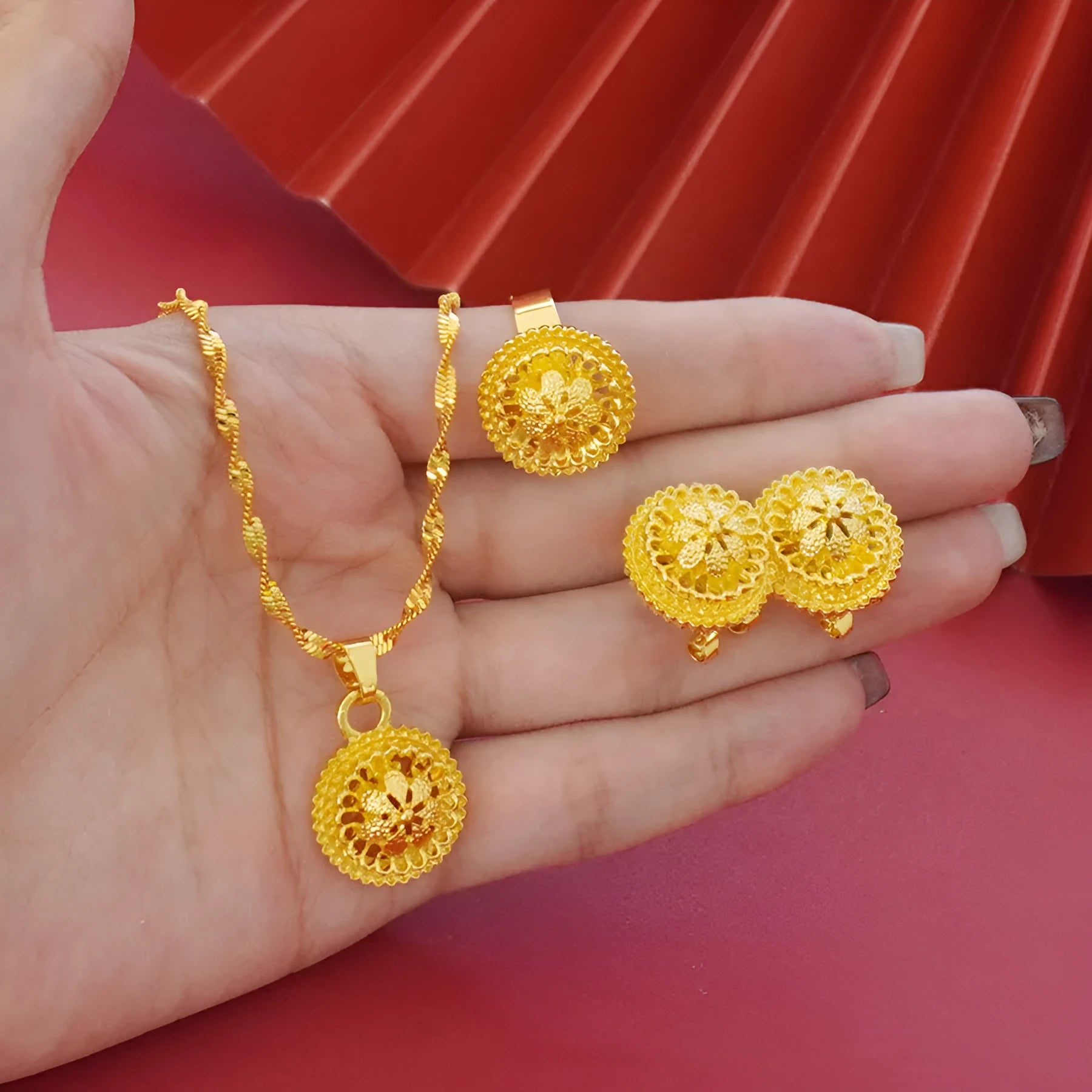 Gold-plated three-piece jewellery set showing necklace with floral pendant, matching earrings, and ring on a grey background.