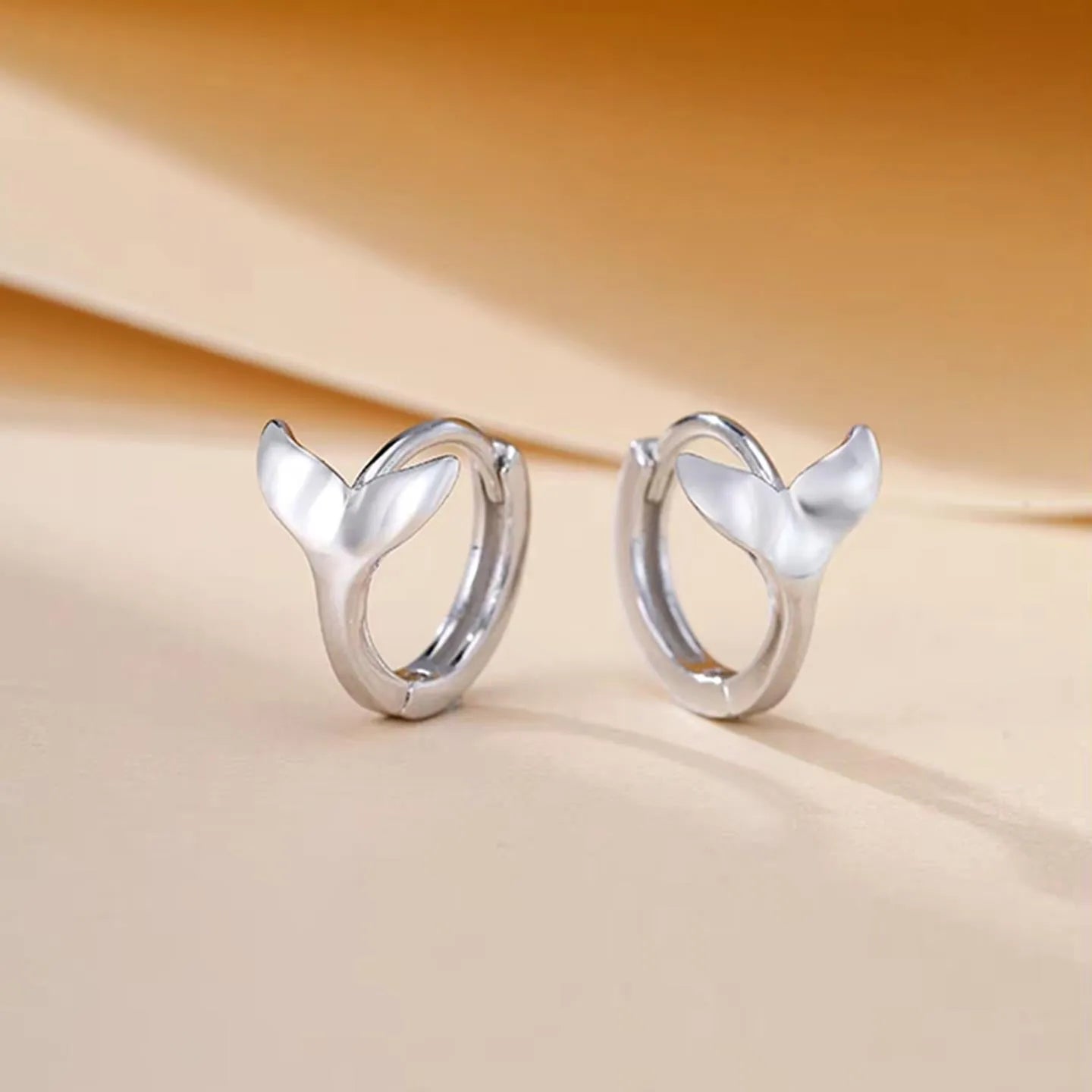 A pair of simple fishtail design earrings with an electroplated metallic finish, shown in white gold and yellow gold colour options.