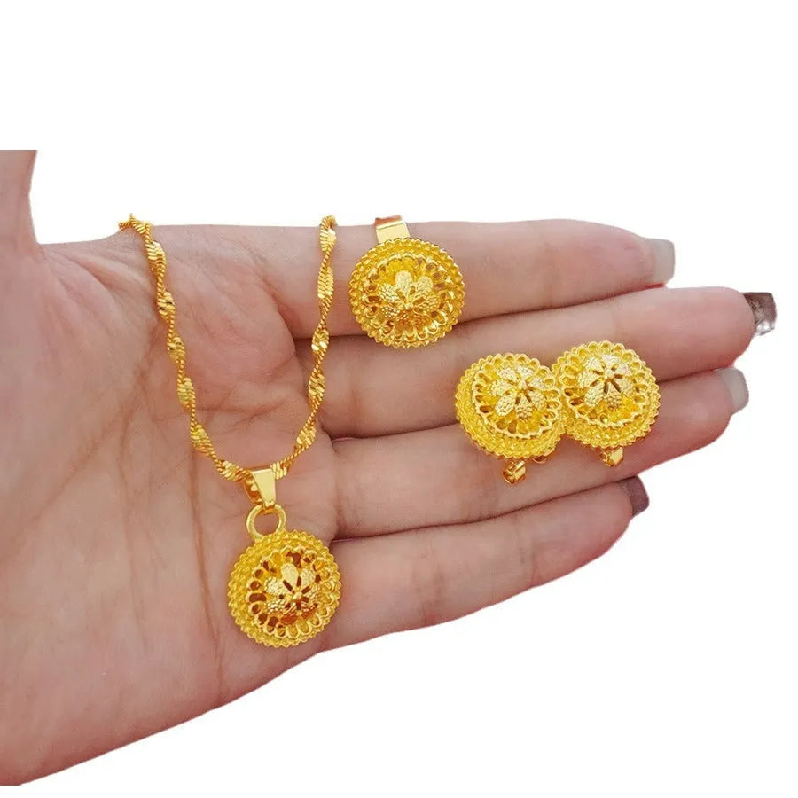 Gold-plated three-piece jewellery set showing necklace with floral pendant, matching earrings, and ring on a grey background.