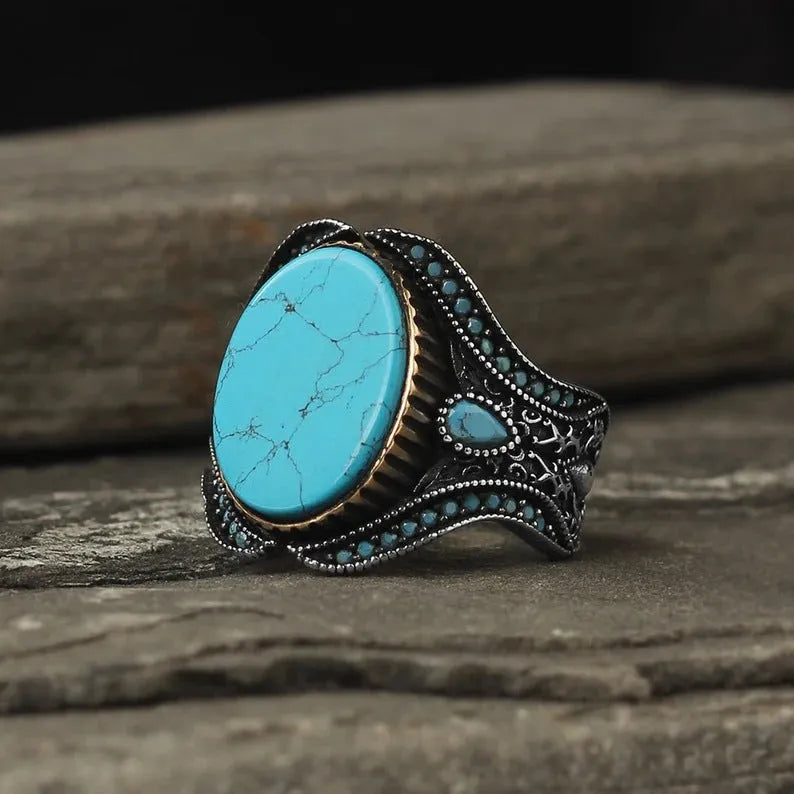A round men's alloy ring in antique silver finish with turquoise colour accents on a plain background.