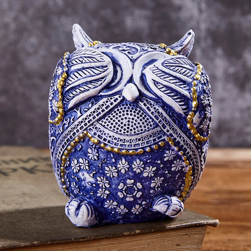 Three blue and white owl resin ornaments with hand-painted pastoral design on wooden surface