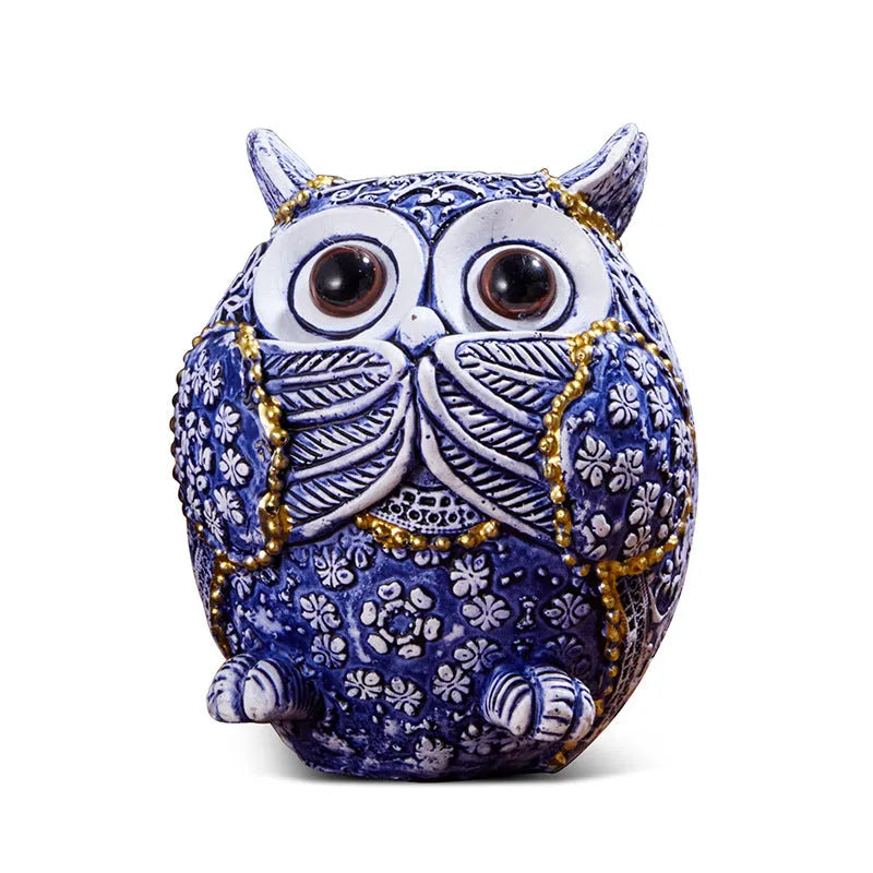 Three blue and white owl resin ornaments with hand-painted pastoral design on wooden surface