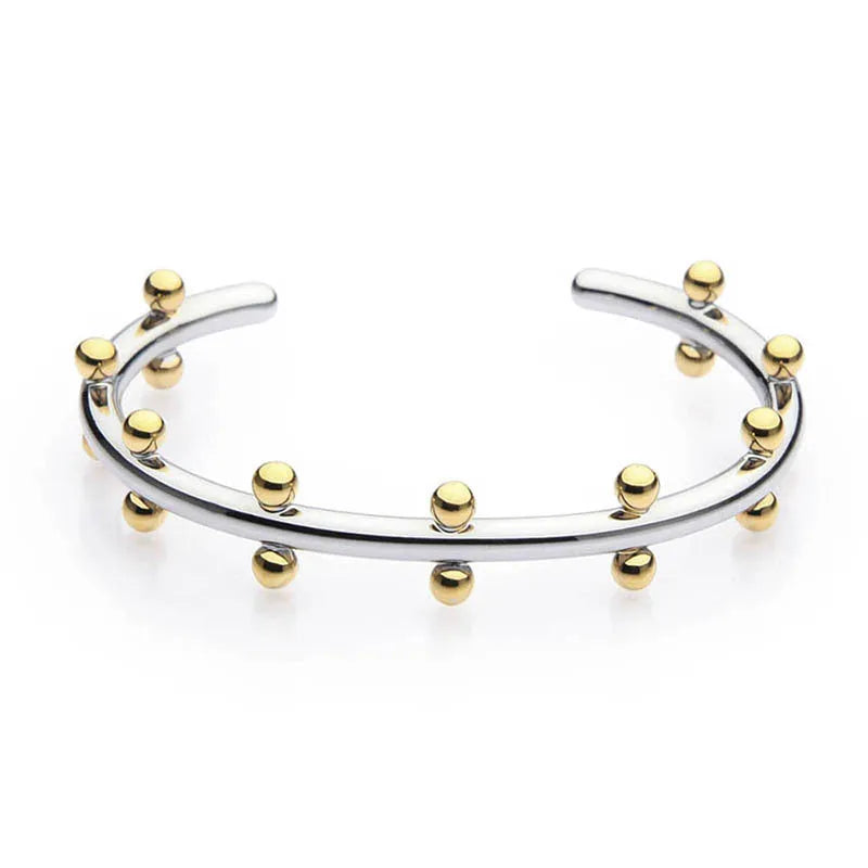 Close-up of a textured stainless steel C-shaped bracelet with rivet-shaped bean beads in a gold finish.