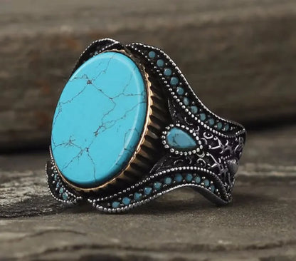 A round men's alloy ring in antique silver finish with turquoise colour accents on a plain background.