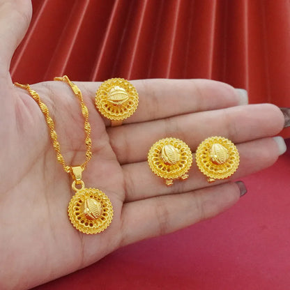 Gold-plated three-piece jewellery set showing necklace with floral pendant, matching earrings, and ring on a grey background.