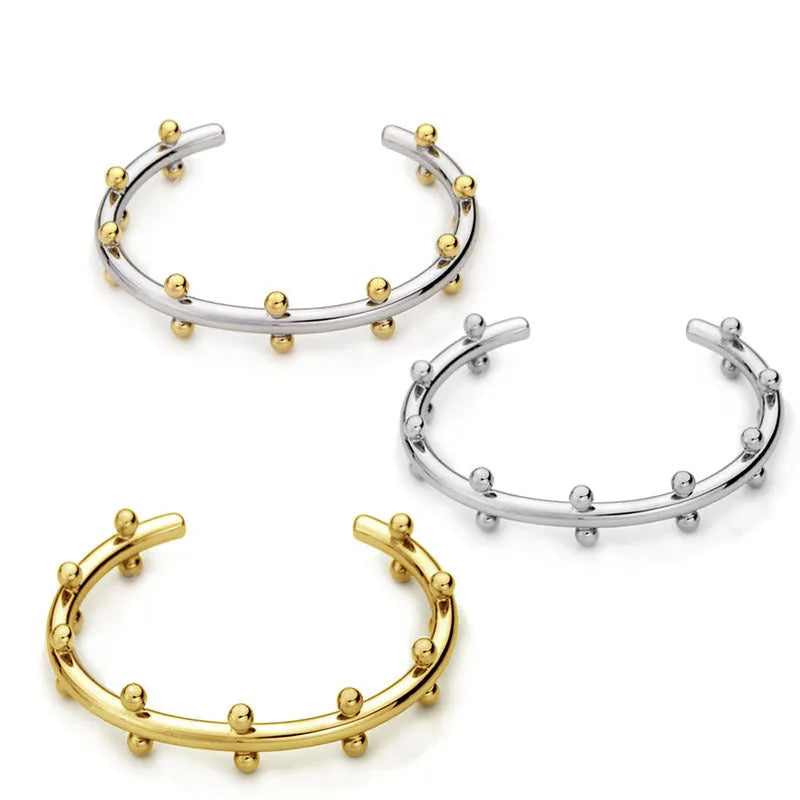 Close-up of a textured stainless steel C-shaped bracelet with rivet-shaped bean beads in a gold finish.