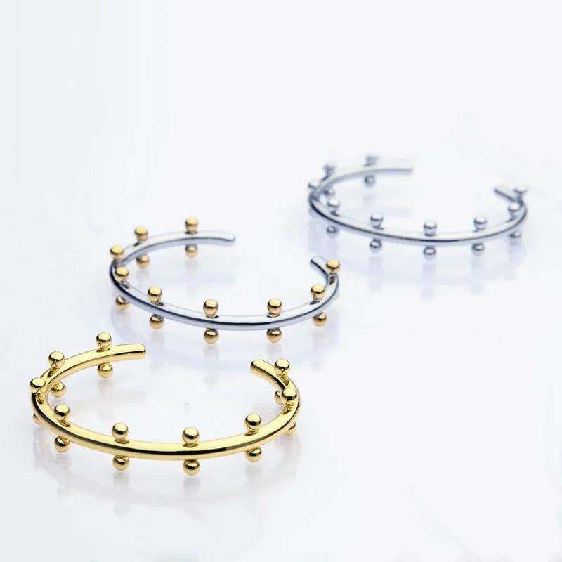 Close-up of a textured stainless steel C-shaped bracelet with rivet-shaped bean beads in a gold finish.