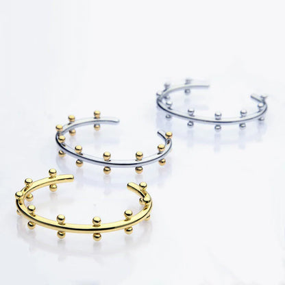 Close-up of a textured stainless steel C-shaped bracelet with rivet-shaped bean beads in a gold finish.
