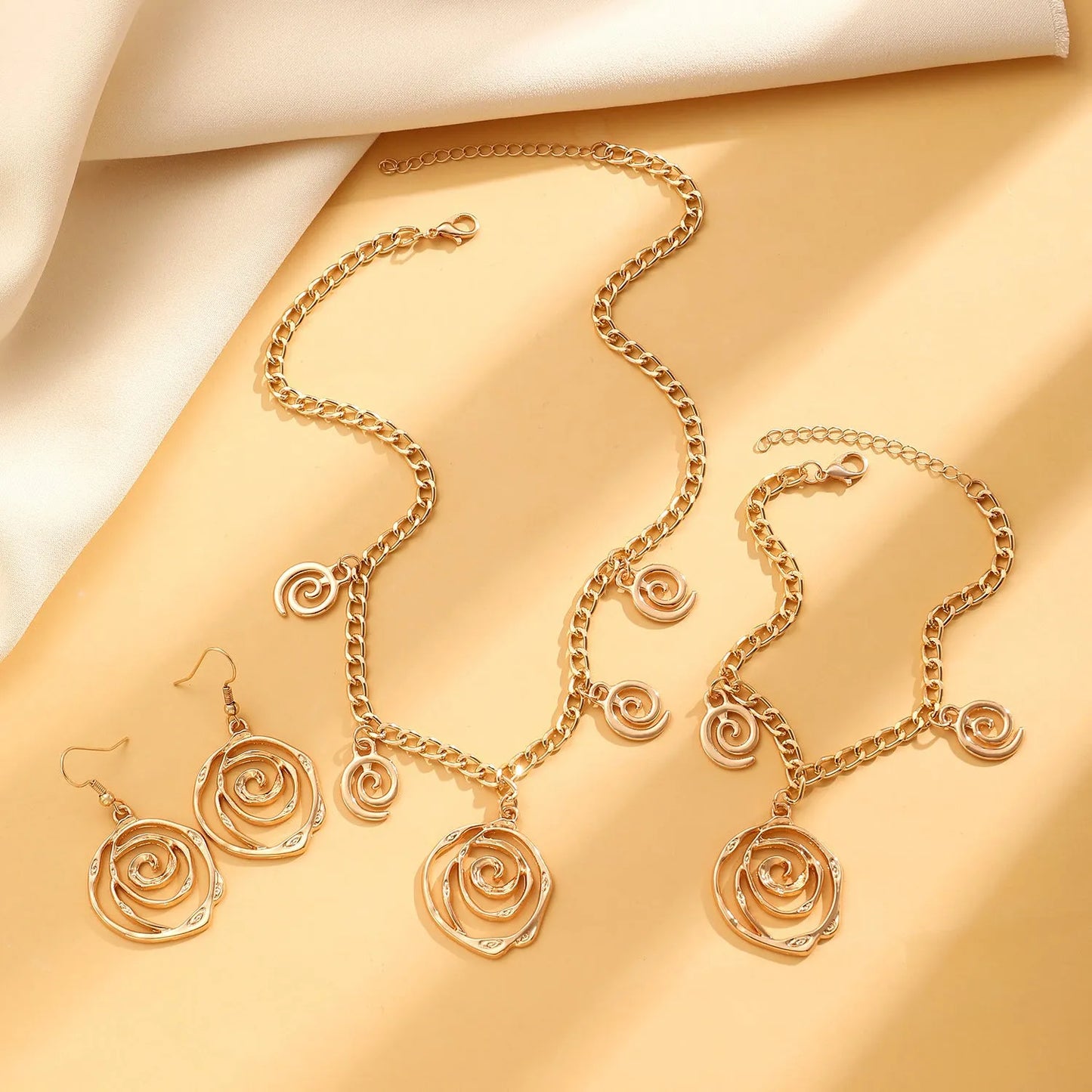 Gold spiral donut alloy jewellery set showing adjustable necklace, matching bracelet, and ear hooks on a plain background.