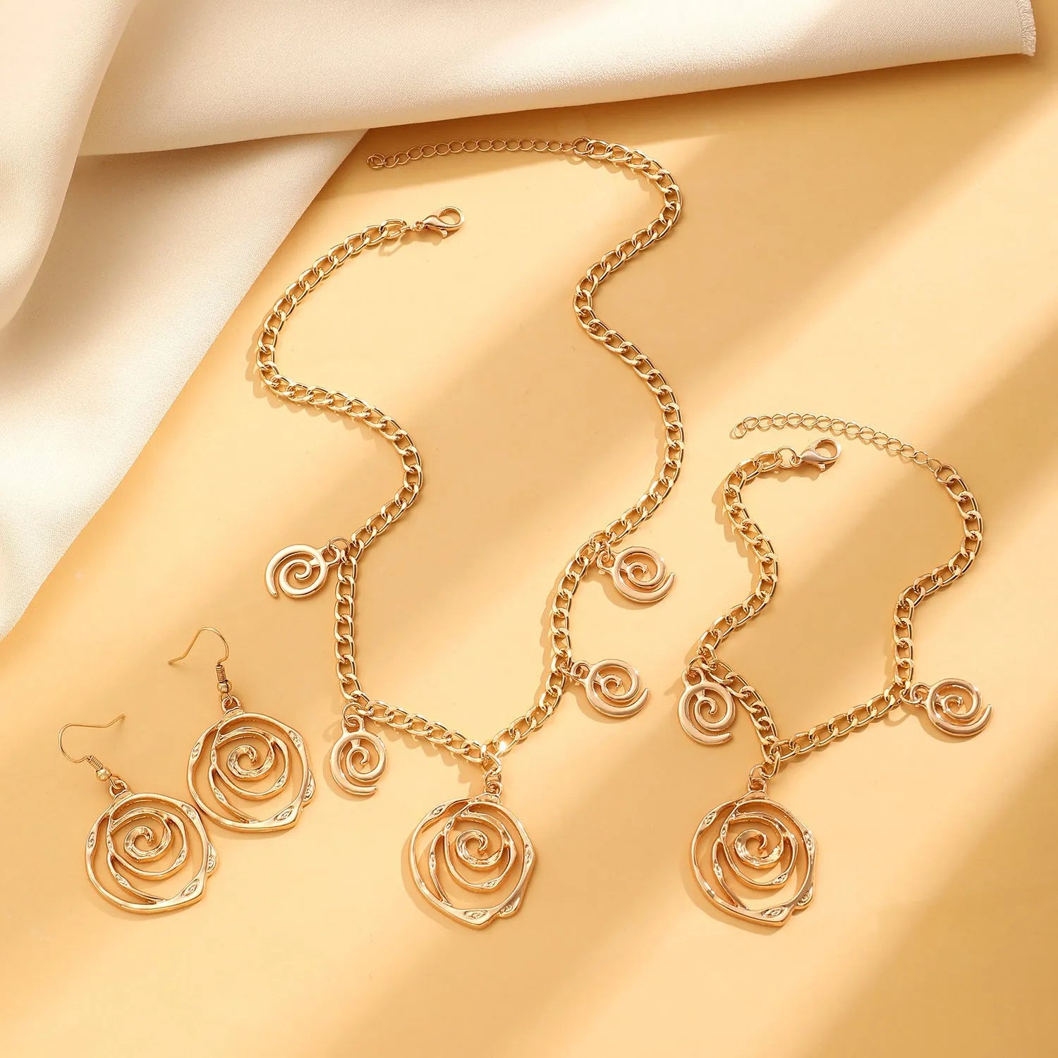 Gold spiral donut alloy jewellery set showing adjustable necklace, matching bracelet, and ear hooks on a plain background.