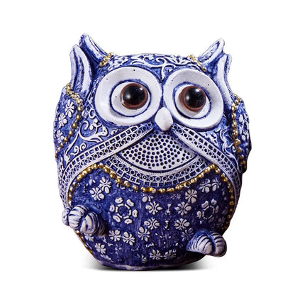 Three blue and white owl resin ornaments with hand-painted pastoral design on wooden surface