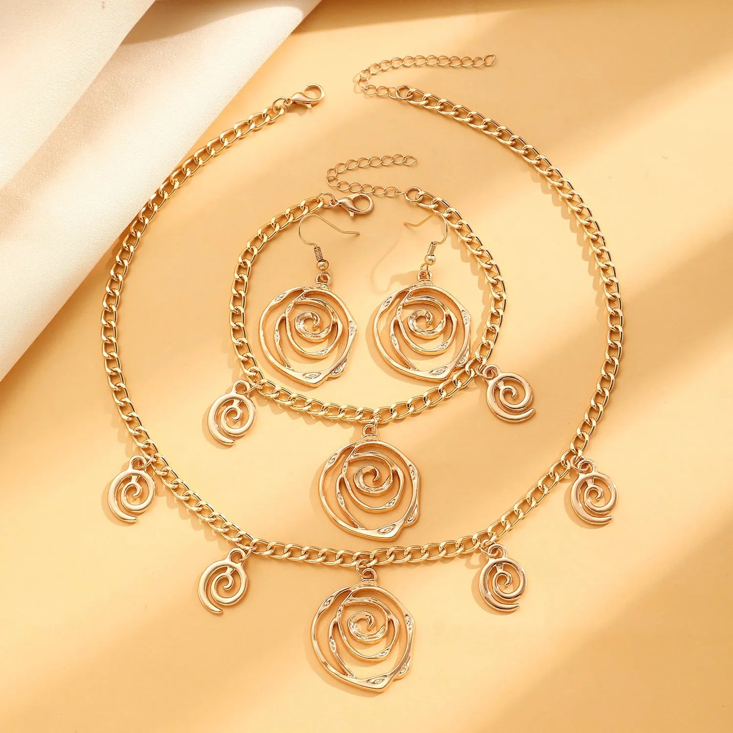 Gold spiral donut alloy jewellery set showing adjustable necklace, matching bracelet, and ear hooks on a plain background.